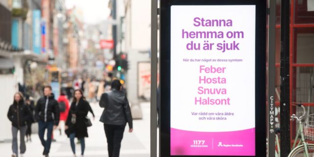 2020年3 月、ストックホルム中心街の歩行者天国。熱・咳・鼻水・のどの痛みのある場合は自宅での休養を呼びかける医療相談サイトのポスター。 写真 Fredrik Sandberg